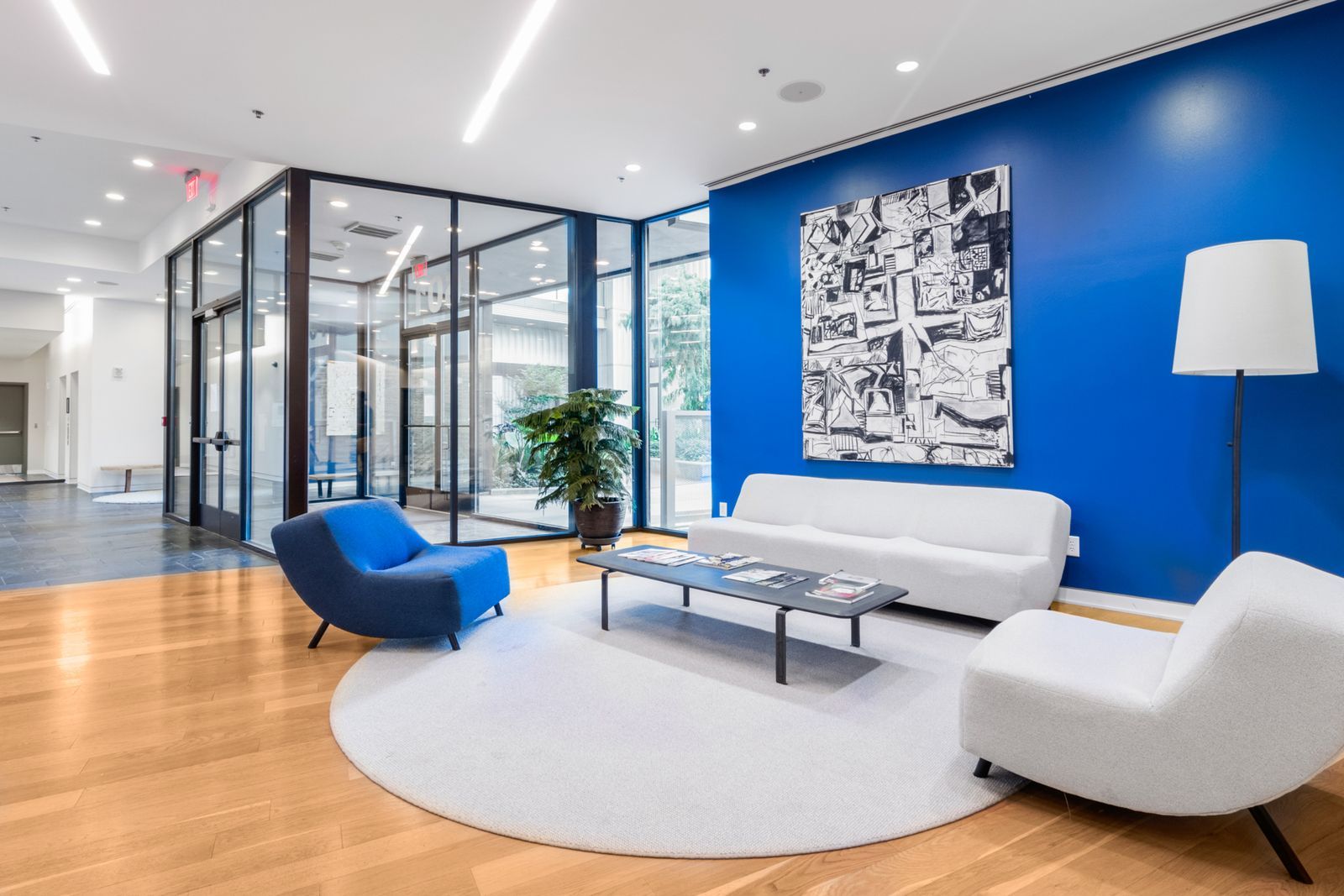 Commercial firm waiting lounge with a reception seating group, glass office partitions, and an abstract hang on a navy wall