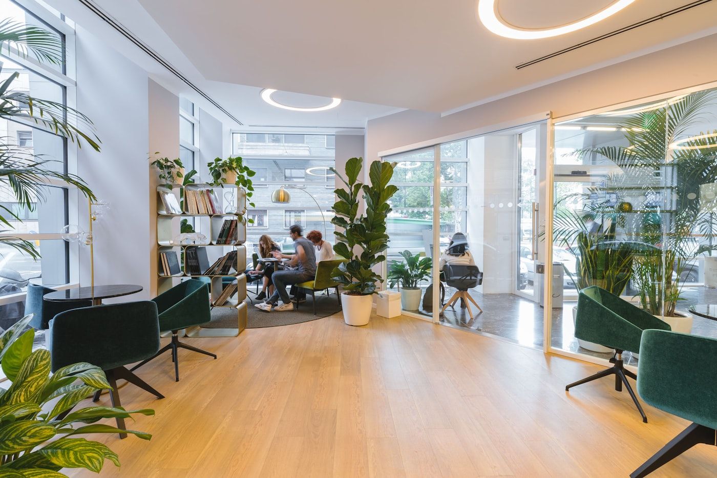 Commercial office lounge with green waiting chairs, glass partitions, and a city street beyond